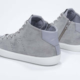 Vista posteriore a tre quarti del modello mid top grigio chiaro sneaker con tomaia in pelle scamosciata con logo a corona traforato, zip interna e suola bianca.