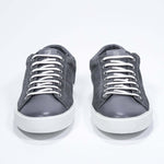Vue de face de la chaussure basse gris foncé sneaker avec logo perforé sur la tige. Tige en daim et semelle en caoutchouc blanc.