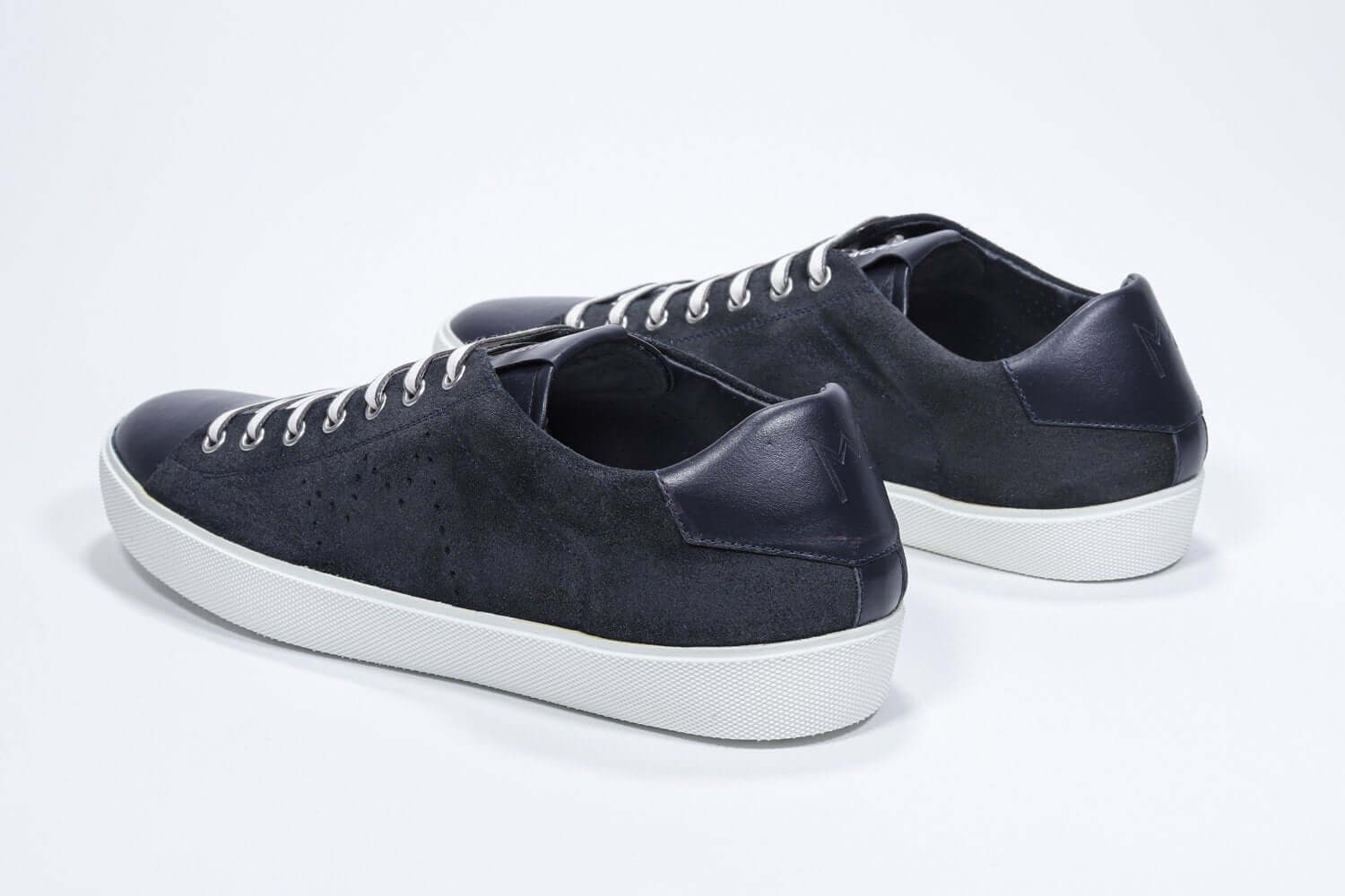 Vue de trois quarts arrière de la chaussure basse marine sneaker avec le logo perforé de la couronne sur la tige. Tige en daim et semelle en caoutchouc blanc.