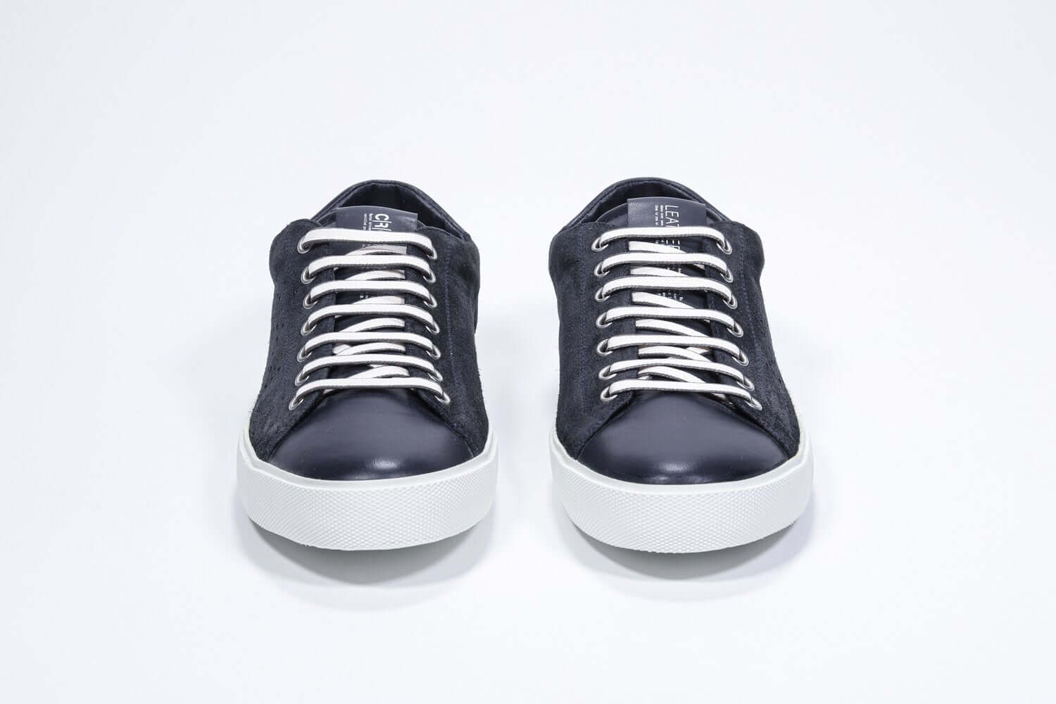 Vue avant de la chaussure basse marine sneaker avec le logo perforé de la couronne sur la tige. Tige en daim et semelle en caoutchouc blanc.