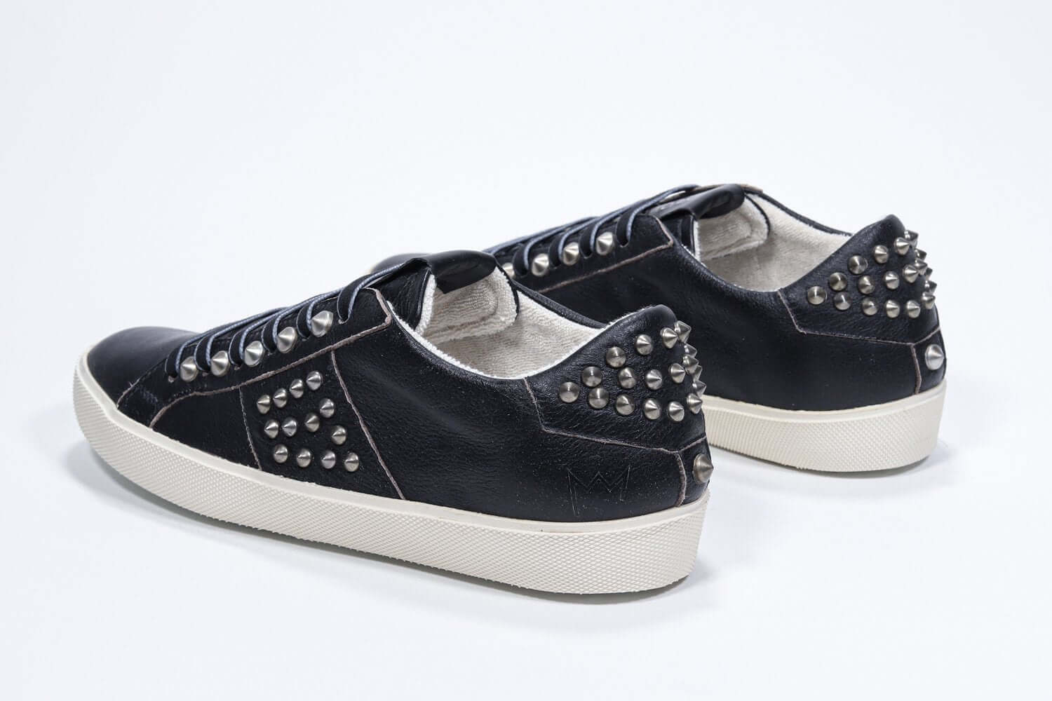 Vue de trois quarts arrière d'un modèle bas noir sneaker. Tige en cuir avec clous et semelle en caoutchouc vintage.