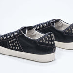 Vue de trois quarts arrière d'un modèle bas noir sneaker. Tige en cuir avec clous et semelle en caoutchouc vintage.