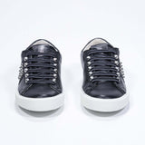 Front view of low top black sneaker. Full grain leather upper with silver studs and antique white rubber sole.