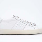 Side view of low top white sneaker. Full grain leather upper with white studs and antique white rubber sole.