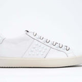 Side view of low top white sneaker. Full grain leather upper with white studs and antique white rubber sole.