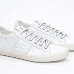 Three quarter front view of low top white sneaker. Full grain leather upper with white studs and antique white rubber sole.