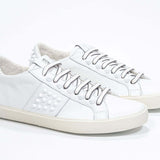 Three quarter front view of low top white sneaker. Full grain leather upper with white studs and antique white rubber sole.