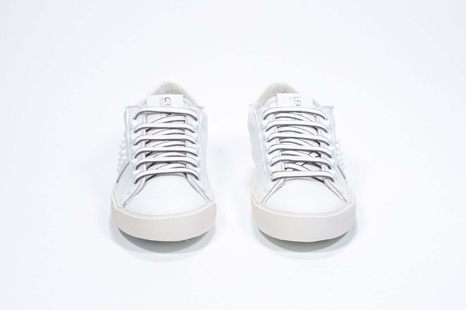 Front view of low top white sneaker. Full grain leather upper with white studs and antique white rubber sole.