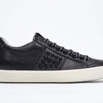 Side view of low top black sneaker. Full grain leather upper with black studs and antique white rubber sole.