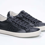 Three quarter view of low top black sneaker. Full grain leather upper with black studs and antique white rubber sole.