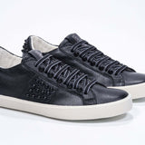 Three quarter view of low top black sneaker. Full grain leather upper with black studs and antique white rubber sole.