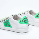 Back view of low top white and fluo green sneaker. Full grain leather upper with gun metal studs and white rubber sole.