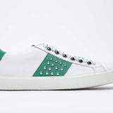 Side profile of low top white and green sneaker. Full grain leather upper with silver studs and white rubber sole.