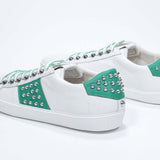 Back view of low top white and green sneaker. Full grain leather upper with silver studs and white rubber sole.