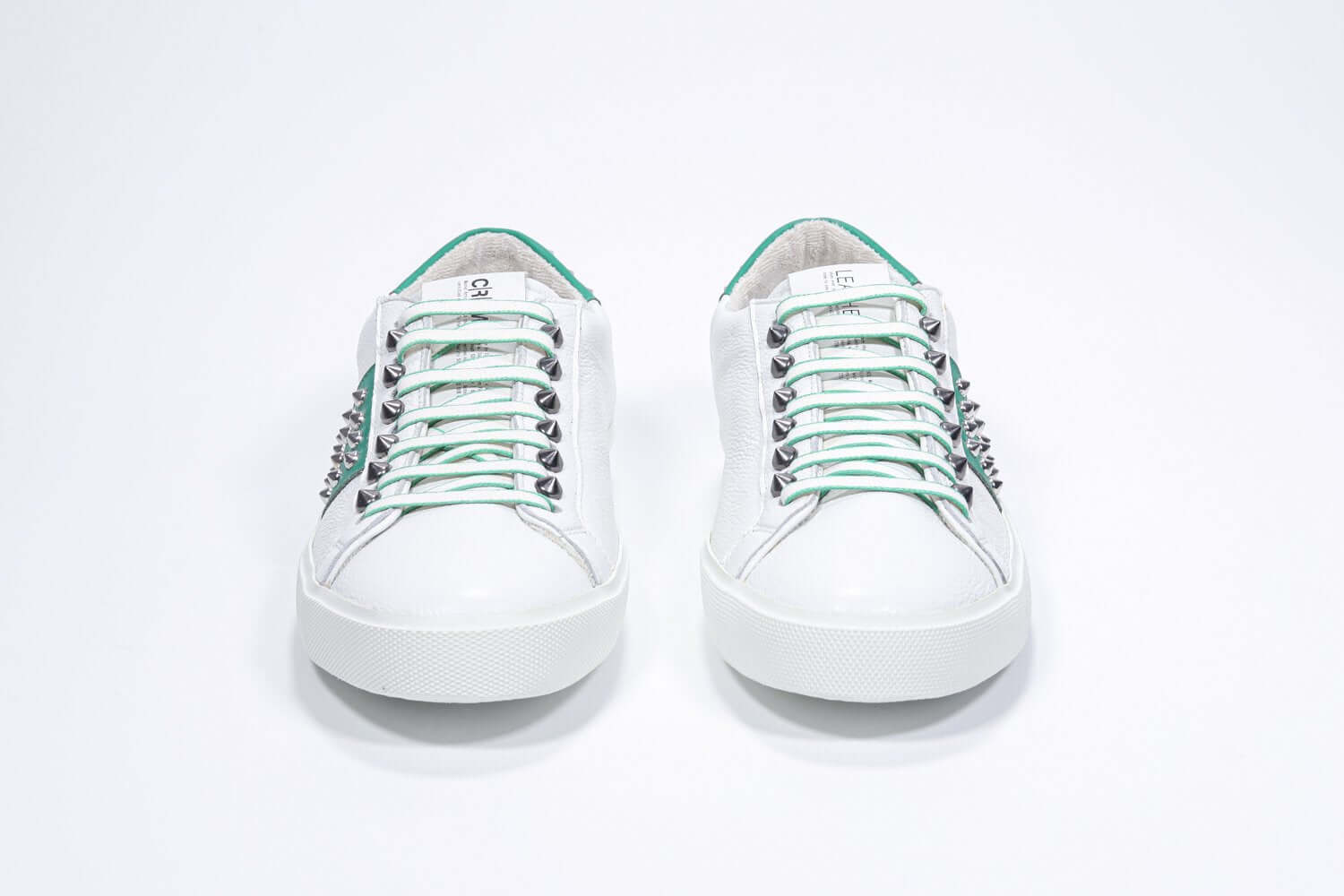 Front view of low top white and green sneaker. Full grain leather upper with silver studs and white rubber sole.