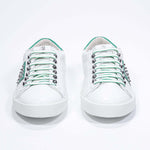 Front view of low top white and green sneaker. Full grain leather upper with silver studs and white rubber sole.