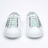 Front view of low top white and green sneaker. Full grain leather upper with silver studs and white rubber sole.