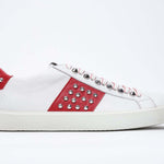 Side profile of low top white and red sneaker. Full grain leather upper with silver studs and white rubber sole.