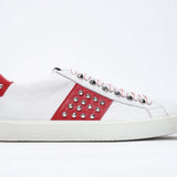 Side profile of low top white and red sneaker. Full grain leather upper with silver studs and white rubber sole.