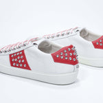 Back view of low top white and red sneaker. Full grain leather upper with silver studs and white rubber sole.