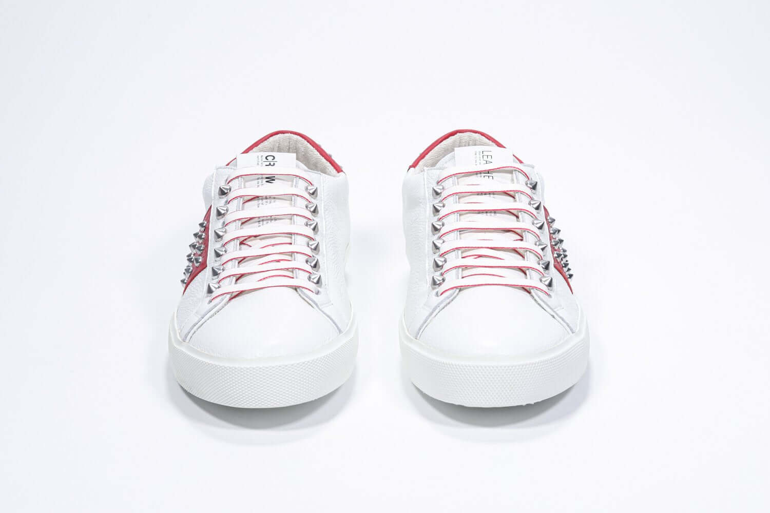 Front view of low top white and red sneaker. Full grain leather upper with silver studs and white rubber sole.