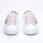 Front view of low top white and red sneaker. Full grain leather upper with silver studs and white rubber sole.