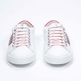Front view of low top white and red sneaker. Full grain leather upper with silver studs and white rubber sole.