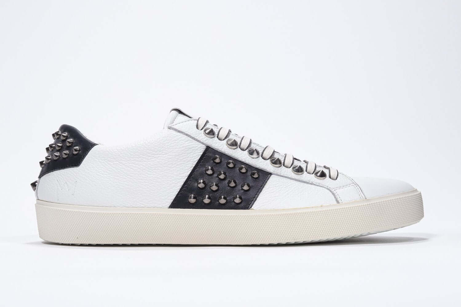Side profile of low top white and navy sneaker. Full grain leather upper with gunmetal studs and vintage rubber sole.