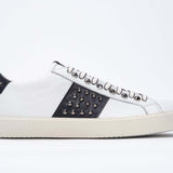 Side profile of low top white and navy sneaker. Full grain leather upper with gunmetal studs and vintage rubber sole.