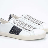 Three quarter front view of low top white and navy sneaker. Full grain leather upper with gunmetal studs and vintage rubber sole.