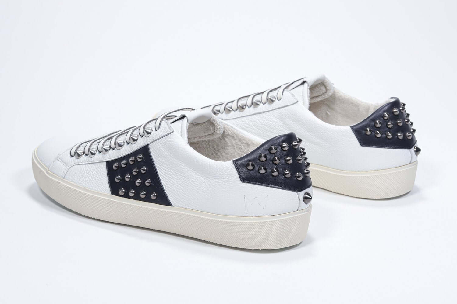 Back view of low top white and navy sneaker. Full grain leather upper with gunmetal studs and vintage rubber sole.
