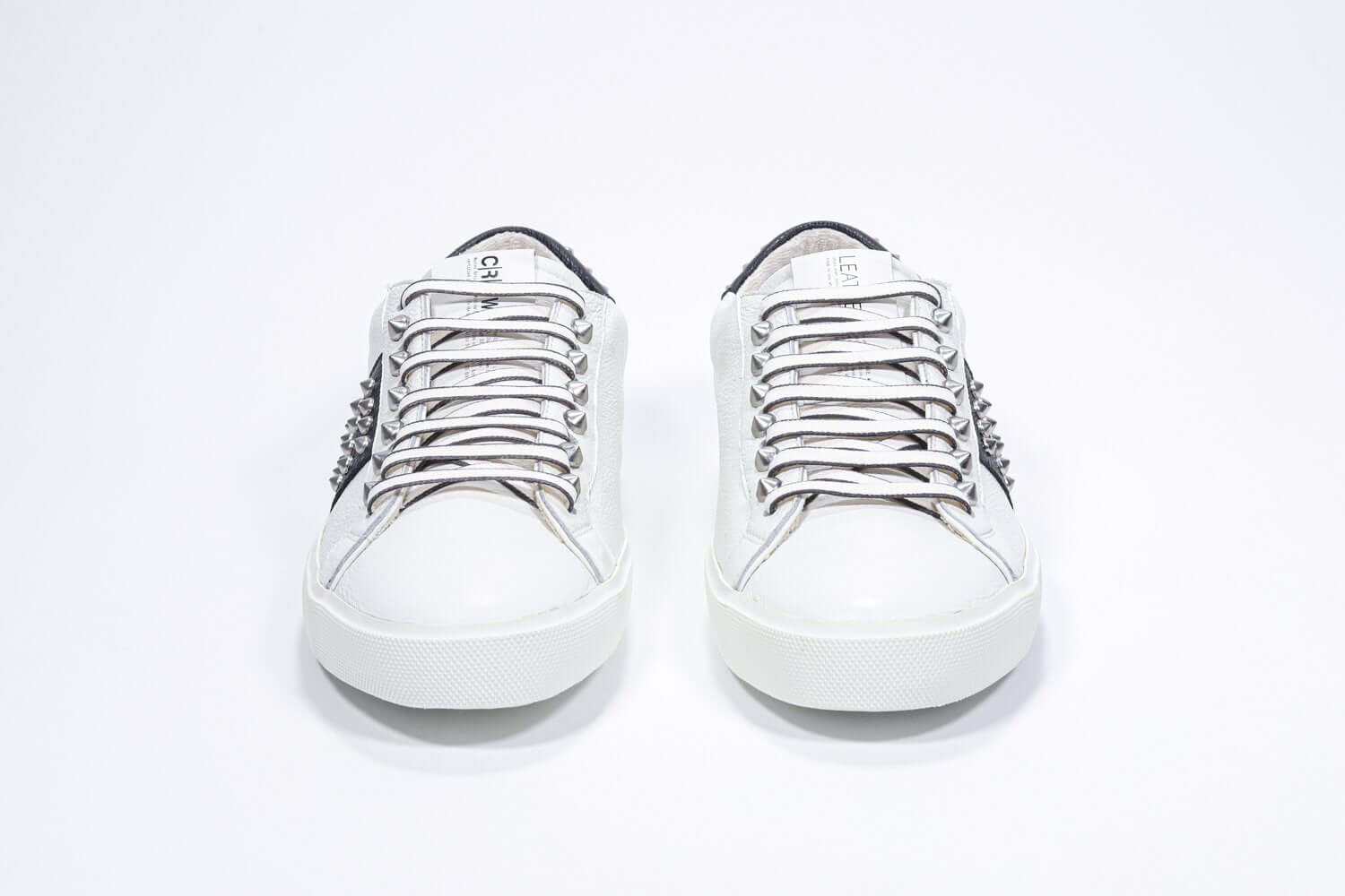 Front view of low top white and navy sneaker. Full grain leather upper with gunmetal studs and vintage rubber sole.