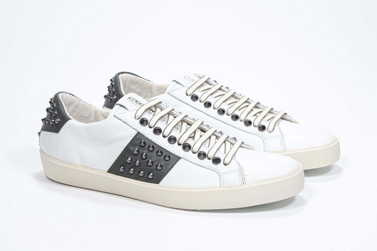 Three quarter front view of low top white and khaki sneaker. Full grain leather upper with gunmetal studs and vintage rubber sole.
