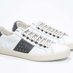 Three quarter front view of low top white and khaki sneaker. Full grain leather upper with gunmetal studs and vintage rubber sole.