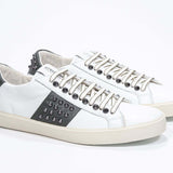 Three quarter front view of low top white and khaki sneaker. Full grain leather upper with gunmetal studs and vintage rubber sole.