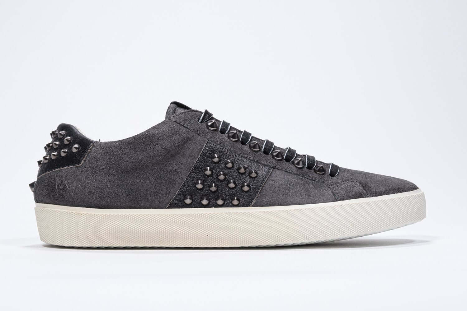 Side profile of low top grey sneaker. Suede upper with gunmetal studs and vintage rubber sole.