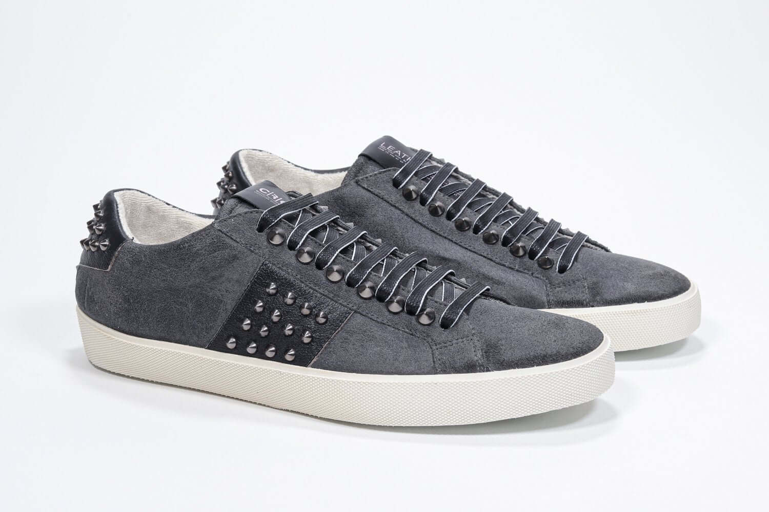 Three quarter front view of low top grey sneaker. Suede upper with gunmetal studs and vintage rubber sole.