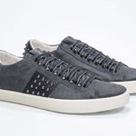 Three quarter front view of low top grey sneaker. Suede upper with gunmetal studs and vintage rubber sole.