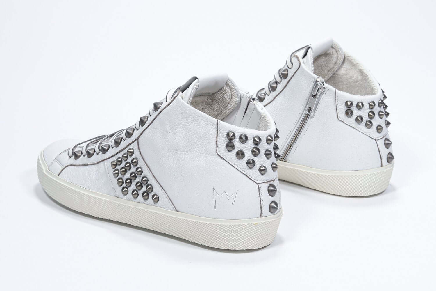 Three quarter back view of mid top white sneaker. Full leather upper with studs, an internal zip and vintage rubber sole.