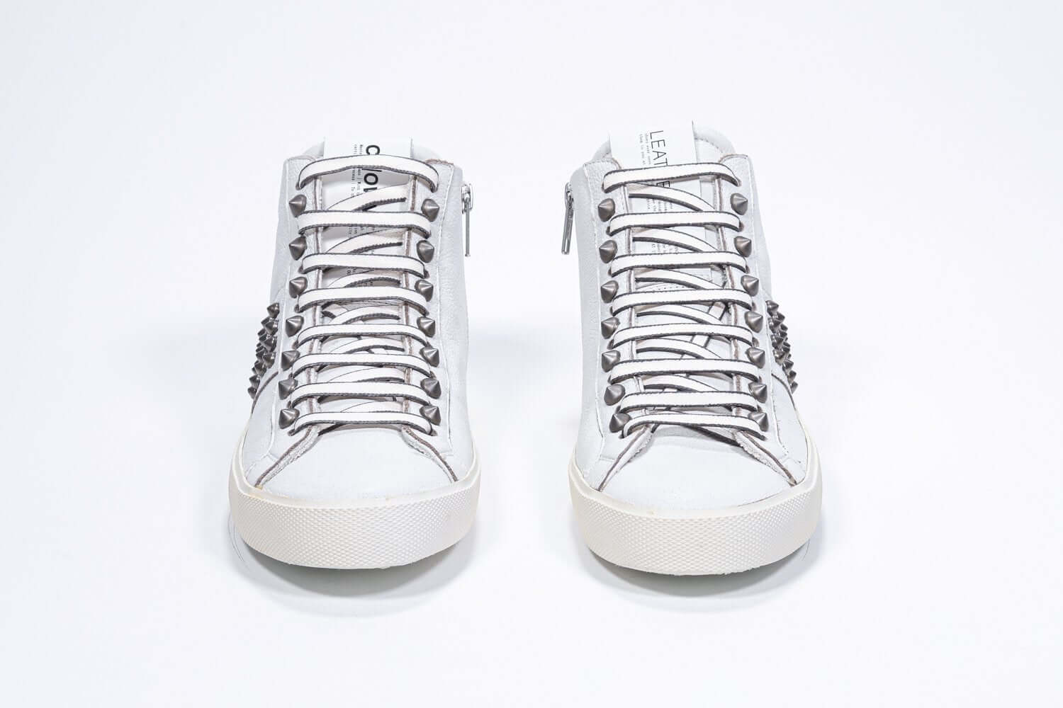 Front view of mid top white sneaker. Full leather upper with studs, an internal zip and vintage rubber sole.