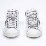 Front view of mid top white sneaker. Full leather upper with studs, an internal zip and vintage rubber sole.