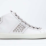 Profilo laterale di mid top bianco sneaker. Tomaia in pelle con borchie, zip interna e suola in gomma bianca.