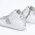 Vista posteriore di tre quarti del modello mid top bianco sneaker. Tomaia in pelle con borchie, zip interna e suola in gomma bianca.