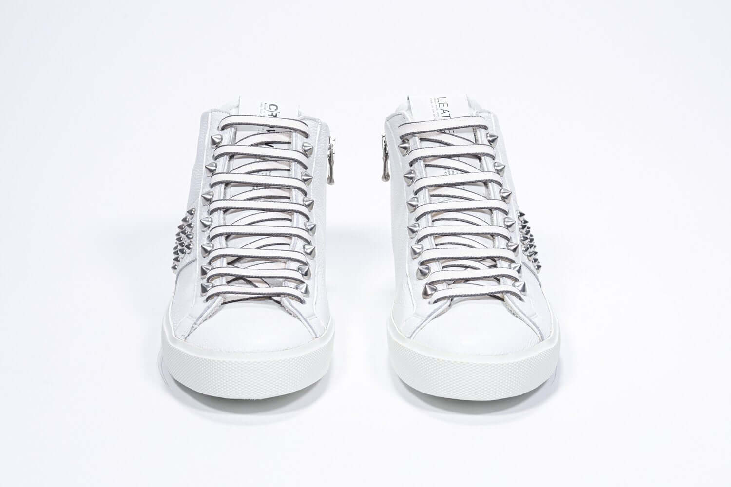 Vista frontale del mid top bianco sneaker. Tomaia in pelle con borchie, zip interna e suola in gomma bianca.