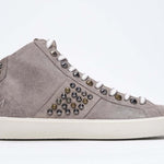 Side profile of mid top beige sneaker. Full suede upper with studs, an internal zip and vintage rubber sole.