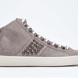 Side profile of mid top beige sneaker. Full suede upper with studs, an internal zip and vintage rubber sole.