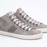 Three quarter front view of mid top beige sneaker. Full suede upper with studs, an internal zip and vintage rubber sole.