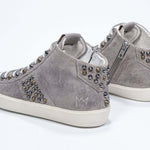 Three quarter back view of mid top beige sneaker. Full suede upper with studs, an internal zip and vintage rubber sole.