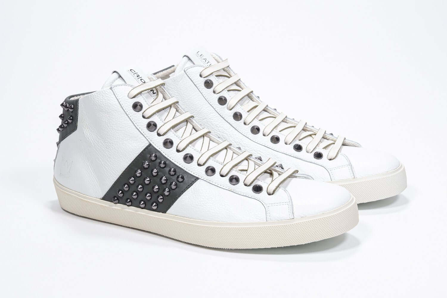 Dreiviertelansicht der Vorderseite von Mid Top weiß und militärgrün sneaker. Obermaterial aus Vollleder mit Nieten, einem internen Reißverschluss und einer Vintage-Gummisohle.