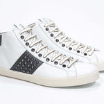 Dreiviertelansicht der Vorderseite von Mid Top weiß und militärgrün sneaker. Obermaterial aus Vollleder mit Nieten, einem internen Reißverschluss und einer Vintage-Gummisohle.